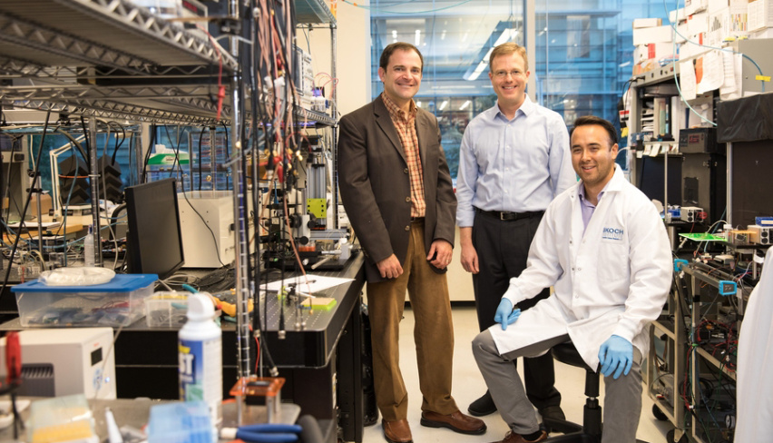 Three men in a lab full of wires and machines.